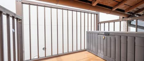 Ein Balkon mit Holzboden, Metallgeländer und Blick zum Himmel.
