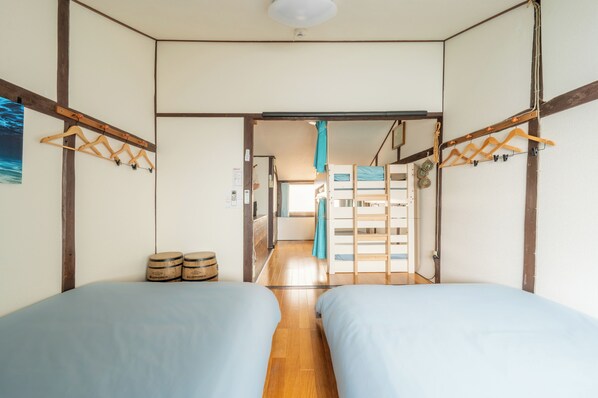 Ein Zimmer mit zwei Betten, Holzbalken, einem Flur und einem Etagenbett im Hintergrund.