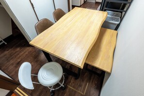 Ein Holztisch mit vier Stühlen, einem weißen Hocker und einem schwarzen Metallregal mit Kunststoffbehältern.
