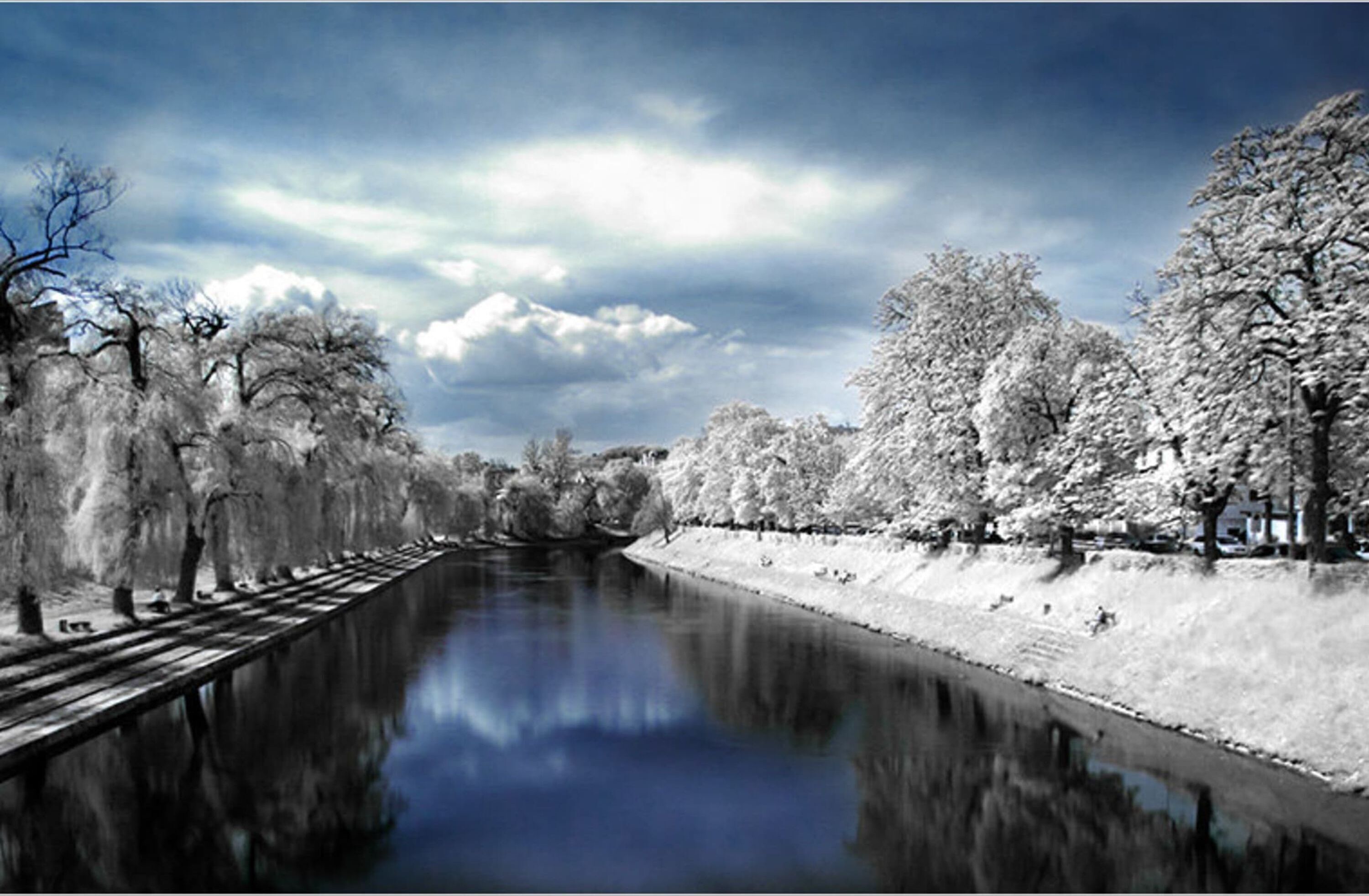 Un río flanqueado por árboles, un puente de madera y un cielo nublado.