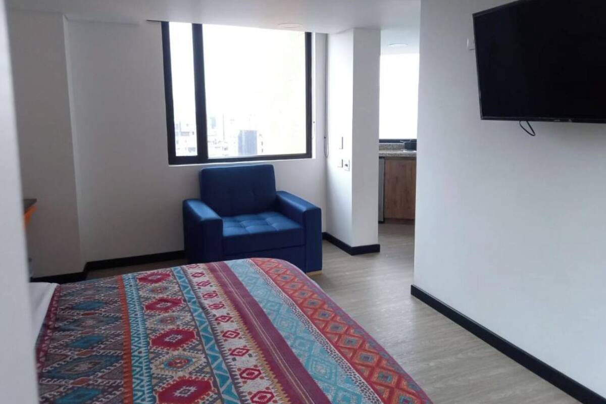 Une chambre d’hôtel avec un lit, une chaise bleue, une télévision, une fenêtre et une vue sur la ville.