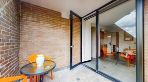 A balcony with a brick wall, a glass door leading to a room, and a small table with a chair. - Terrazas (Bogota)