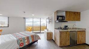 A modern hotel room with a bed, a small kitchenette, a sliding glass door to a balcony, and a city view. - Terrazas (Bogota)