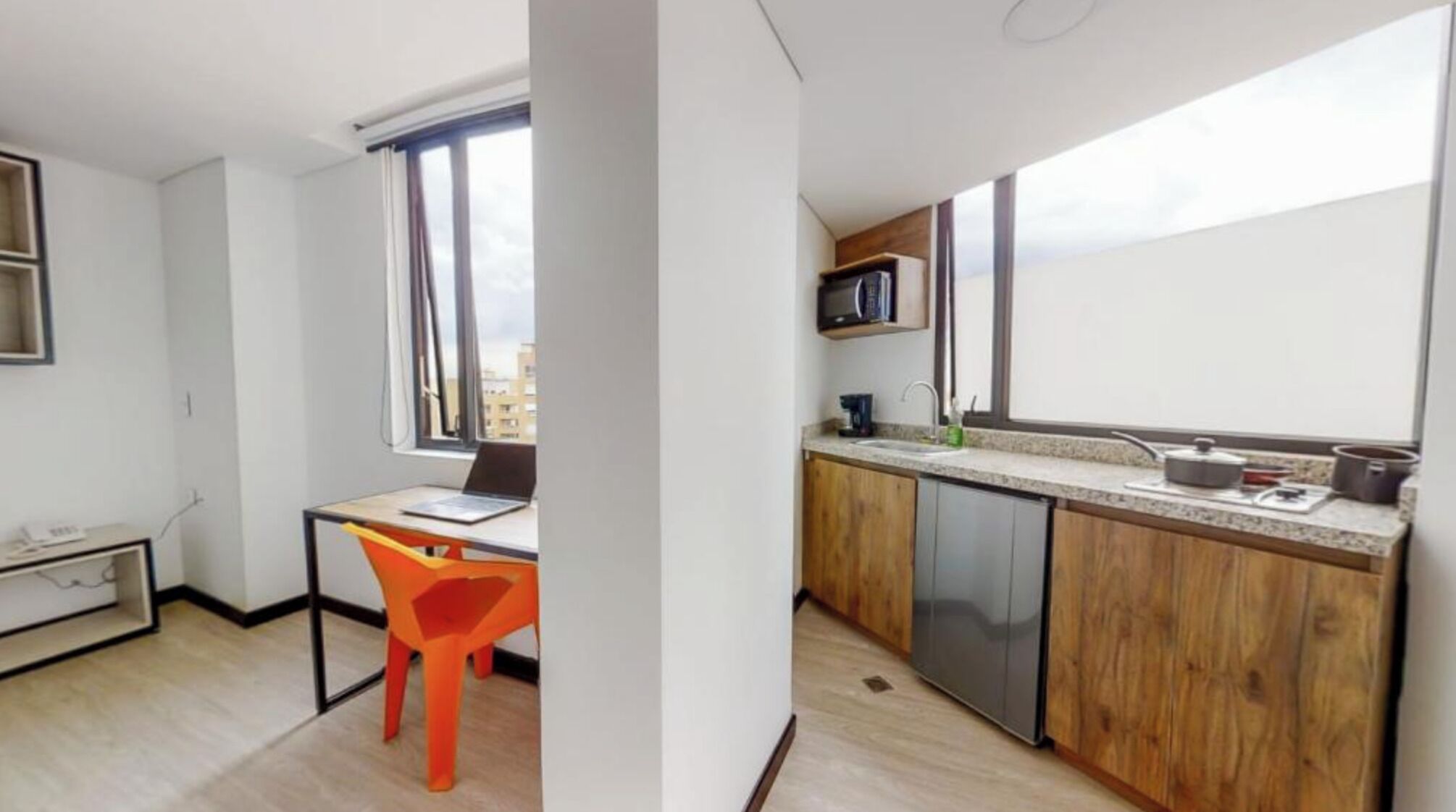 A compact apartment with a kitchenette, a dining area with a chair, and a window providing a view of the city.