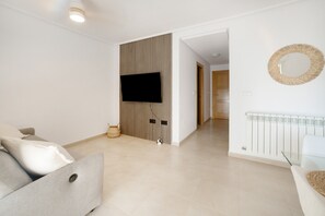 Ein modernes Wohnzimmer mit einem flachbildfernseher an der Wand, einem Sofa und einem Glastisch.