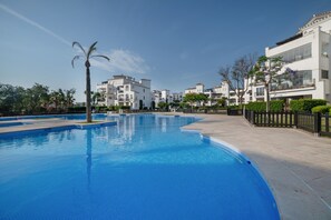 A swimming pool with a curved edge, surrounded by a paved walkway and a fence. - Ground Floor Apartment 'Ullastre' in Torre Golf Resort (Torre-Pacheco)