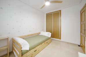 A single bed with a wooden frame and a green mattress, a ceiling fan, a wardrobe, and a wall with triangular decals. - Ground Floor Apartment 'Ullastre' in Torre Golf Resort (Torre-Pacheco)