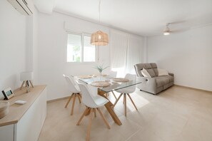 A modern living space with a glass dining table, white chairs, a grey sofa, and a ceiling fan. - Ground Floor Apartment 'Ullastre' in Torre Golf Resort (Torre-Pacheco)