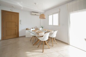 A modern dining area with a glass table, white chairs, a woven pendant light, and a window with sheer curtains. - Ground Floor Apartment 'Ullastre' in Torre Golf Resort (Torre-Pacheco)