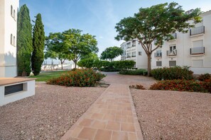 A pathway leading to a building with a white facade, surrounded by greenery and red flowers. - Ground Floor Apartment 'Ullastre' in Torre Golf Resort (Torre-Pacheco)