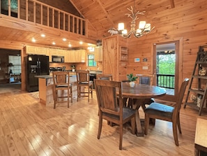 A wooden cabin interior with a dining area, kitchen, and a balcony with a view. - A Bear's Eye View - Pet Friendly | Mountain View | Hot Tub | Game Room (Blue Ridge)
