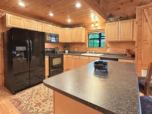 A kitchen with wooden cabinets, a black refrigerator, a microwave, a stove, and a sink. - A Bear's Eye View - Pet Friendly | Mountain View | Hot Tub | Game Room (Blue Ridge)