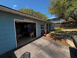 Un bâtiment bleu avec une porte de garage ouverte, dévoilant un espace patio aménagé avec des meubles d’extérieur et une petite table.