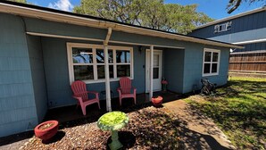 A house with a covered porch, two red Adirondack chairs, a small garden with a birdbath, and a gravel pathway. - Peaceful 3-bedroom getaway in charming Lamar, TX (Rockport)