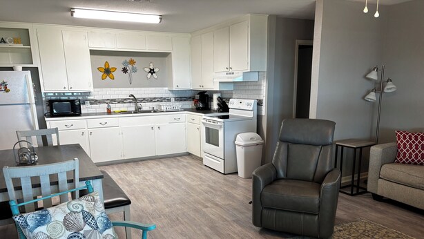 A modern kitchen with white cabinets, a microwave, and a stove. There is a dining table with chairs, a sofa, and a patterned rug. - Peaceful 3-bedroom getaway in charming Lamar, TX (Rockport)
