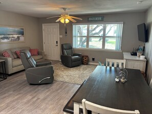 Una sala de estar con sofá, sillón reclinable, mesa de comedor y ventilador de techo.