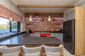 Una cocina con pared de ladrillo, una isla grande con sillas, lámparas colgantes y electrodomésticos modernos.