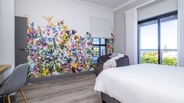 Ein Schlafzimmer mit einem großen Bett, einem Sessel, einer farbenfrohen Blütenwand und einem Fenster mit Blick.