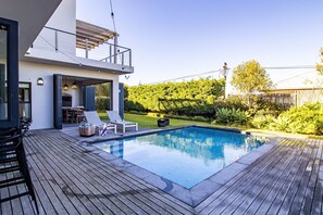 Ein modernes Haus mit Swimmingpool, Gartenmöbeln und einem gepflegten Garten.