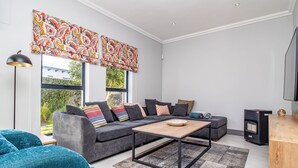 Ein modernes Wohnzimmer mit einem grauen Sofa, Türkis-Armstühlen, einem Holztisch und einem großen Fenster mit gemusterten Vorhängen.