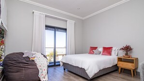 Ein Schlafzimmer mit einem Bett, einem Sitzsack, einem Nachttisch aus Holz und einem Fenster mit Vorhängen.
