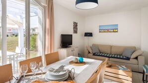 A room with a dining table set for four, a sofa, a television, and a view of the outside. - Maritime Sanctuary in the Vendee (Talmont-Saint-Hilaire)