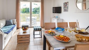 A dining area with a table set for a meal, a sofa, a television, and a view of the outdoors. - Maritime Sanctuary in the Vendee (Talmont-Saint-Hilaire)
