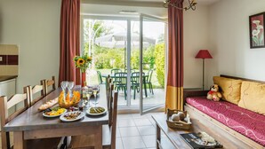 A dining area with a table set for two, a sofa with cushions, and a window with curtains. - Duplex Maisonette in Dordogne (Bergerac)
