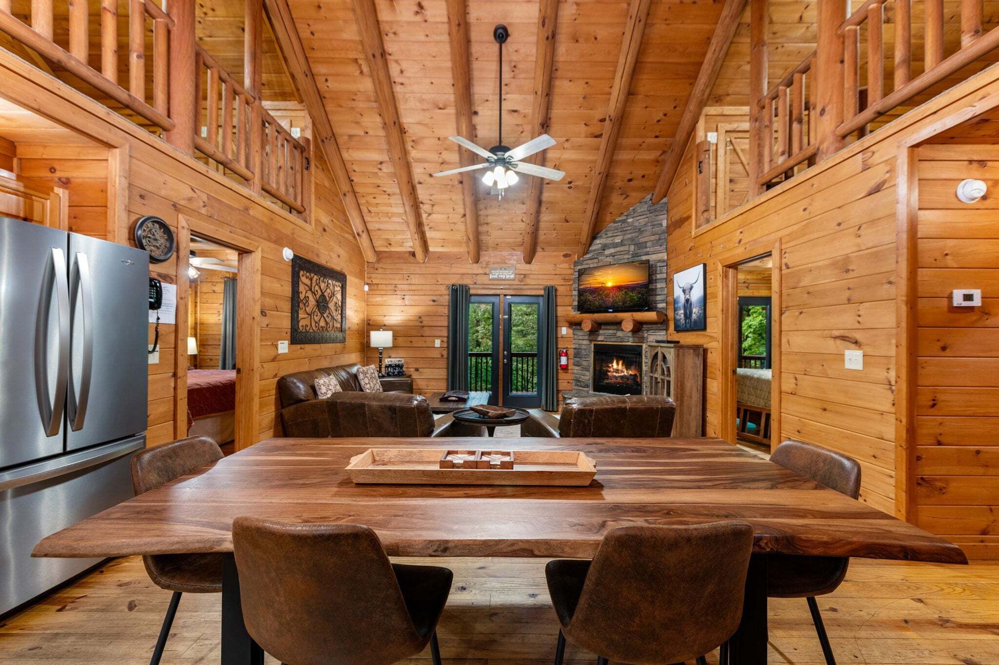 L’intérieur d’un chalet en bois comprend une table à manger, des chaises, un réfrigérateur, une cheminée et un ventilateur de plafond.