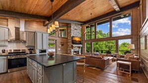 A spacious kitchen with a large island, built-in appliances, and a stone fireplace. - The Day Hike - Pet Friendly | Mountain View | Outdoor Fireplace | Oversized Deck (Blue Ridge)