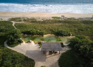 Une vue aérienne d’une plage avec une petite construction, un chemin dégagé et une étendue d’eau.