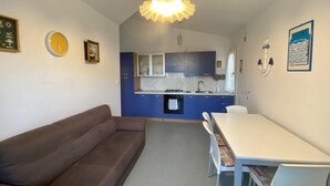 Eine moderne Küche mit blauen Schränken, einem Esstisch mit Stühlen, einer Couch und einer Pendelleuchte.