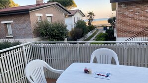 Ein Balkon mit weißen Stühlen und einem Tisch, mit Blick auf Strand und Häuser.