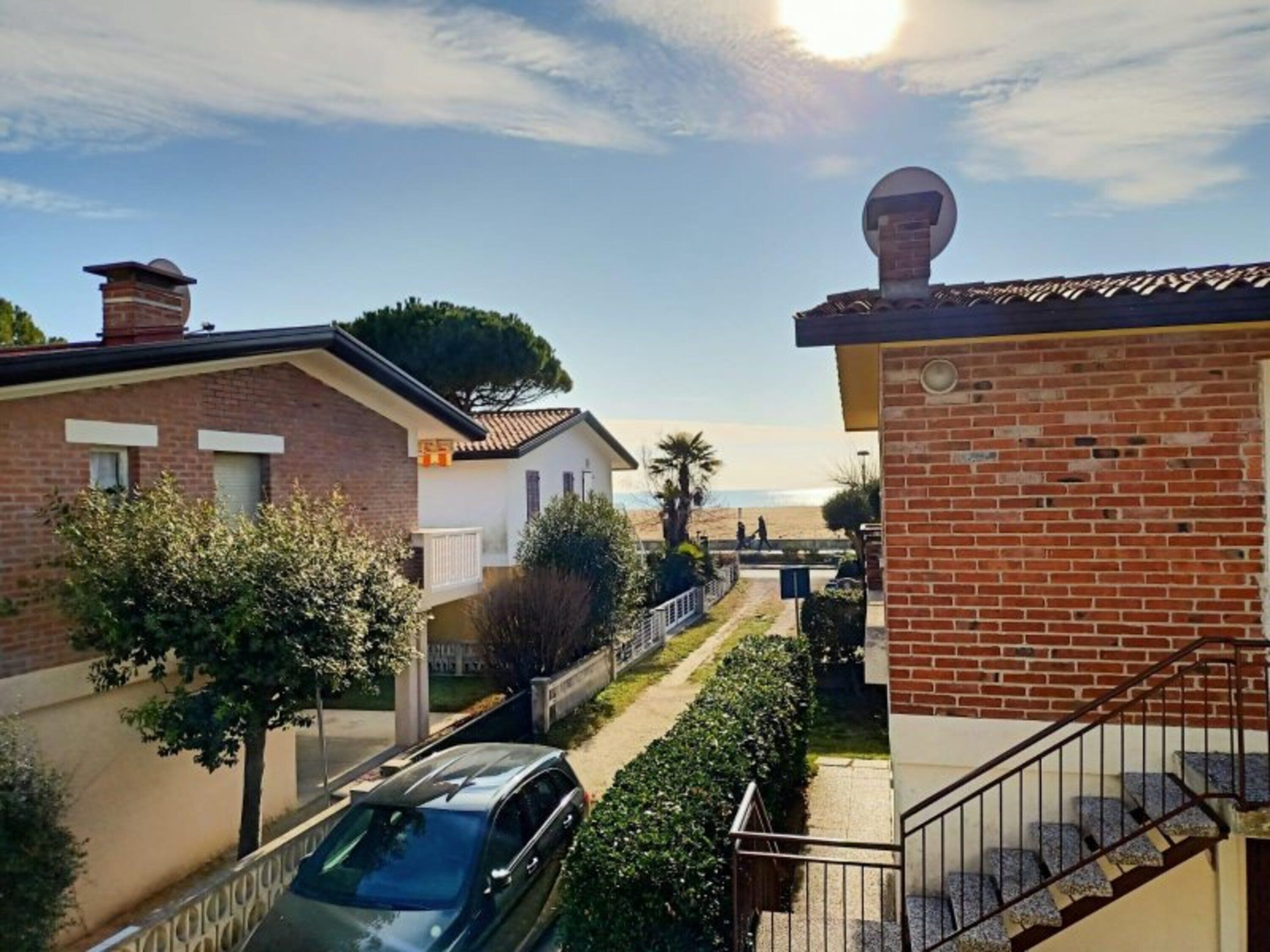 A residential area with brick houses, a car parked on the street, and a clear view of the beach in the background.
