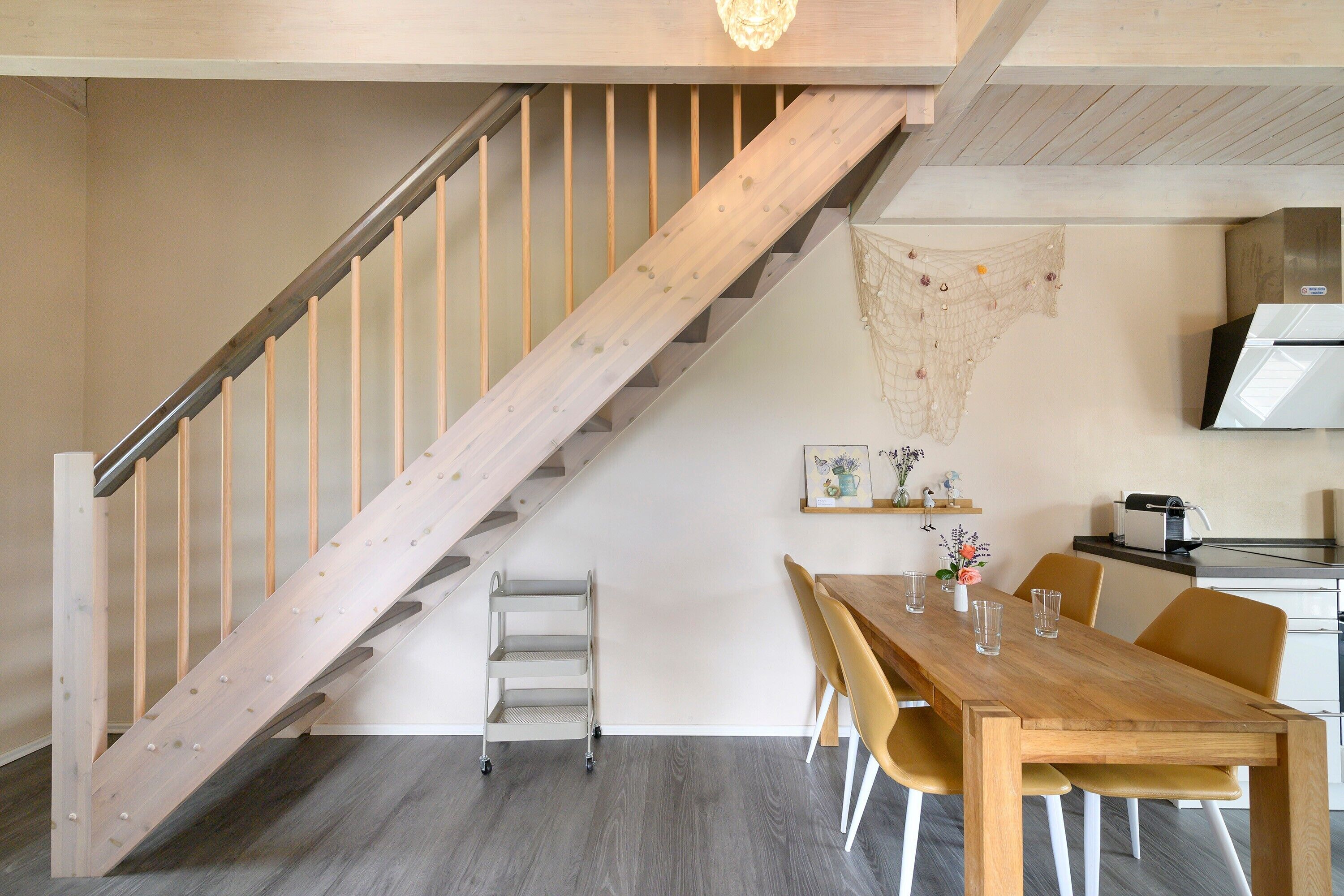 Un escalier avec une rampe en bois, un coin repas avec une table et des chaises en bois, et une cuisine équipée.