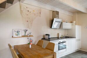 Una cocina con mesa de madera, sillas, estufa y refrigerador.