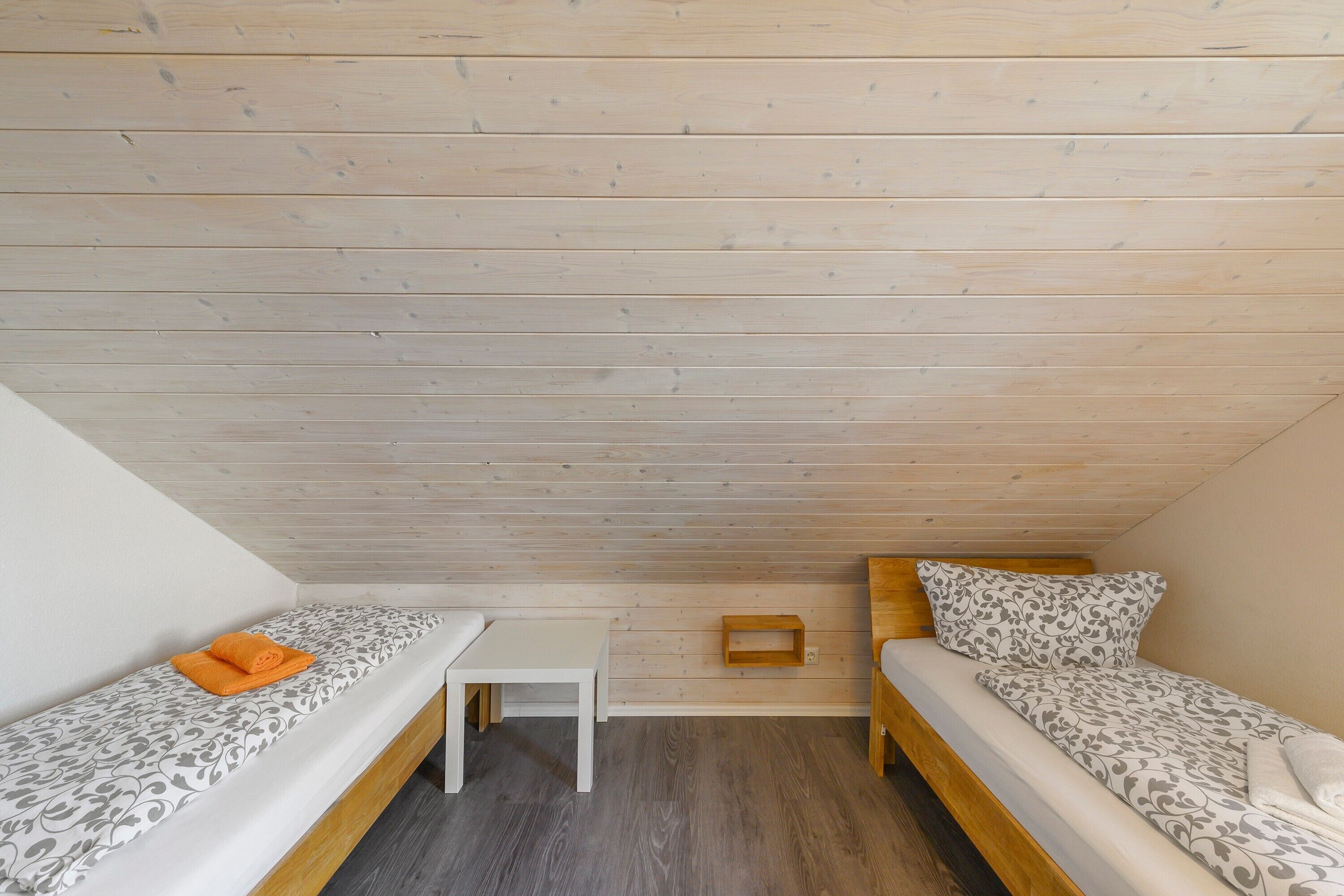 A small, cozy room with two beds, a small table, and a wooden ceiling.