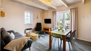 Een woonkamer met een bank, een eettafel, een televisie en een raam met gordijnen.