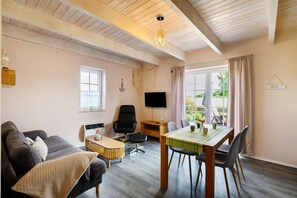 A living room with a sofa, a dining table, a TV, and a window with curtains. - Swedish Cottage Zierow - Baltic Sea - House 16b (Zierow)