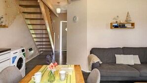 Een woonkamer met een bank, een bijzettafeltje met een boek en een mok, een wasmachine, en een trap naar een andere kamer.