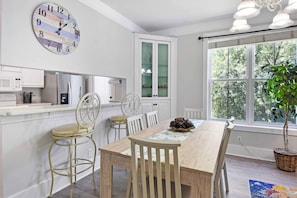 A dining area with a wooden table, chairs, a clock, and a window with a view of trees. - 3 bedroom two bath with a community pool. Sleeps 7. (Saint Simons Island)