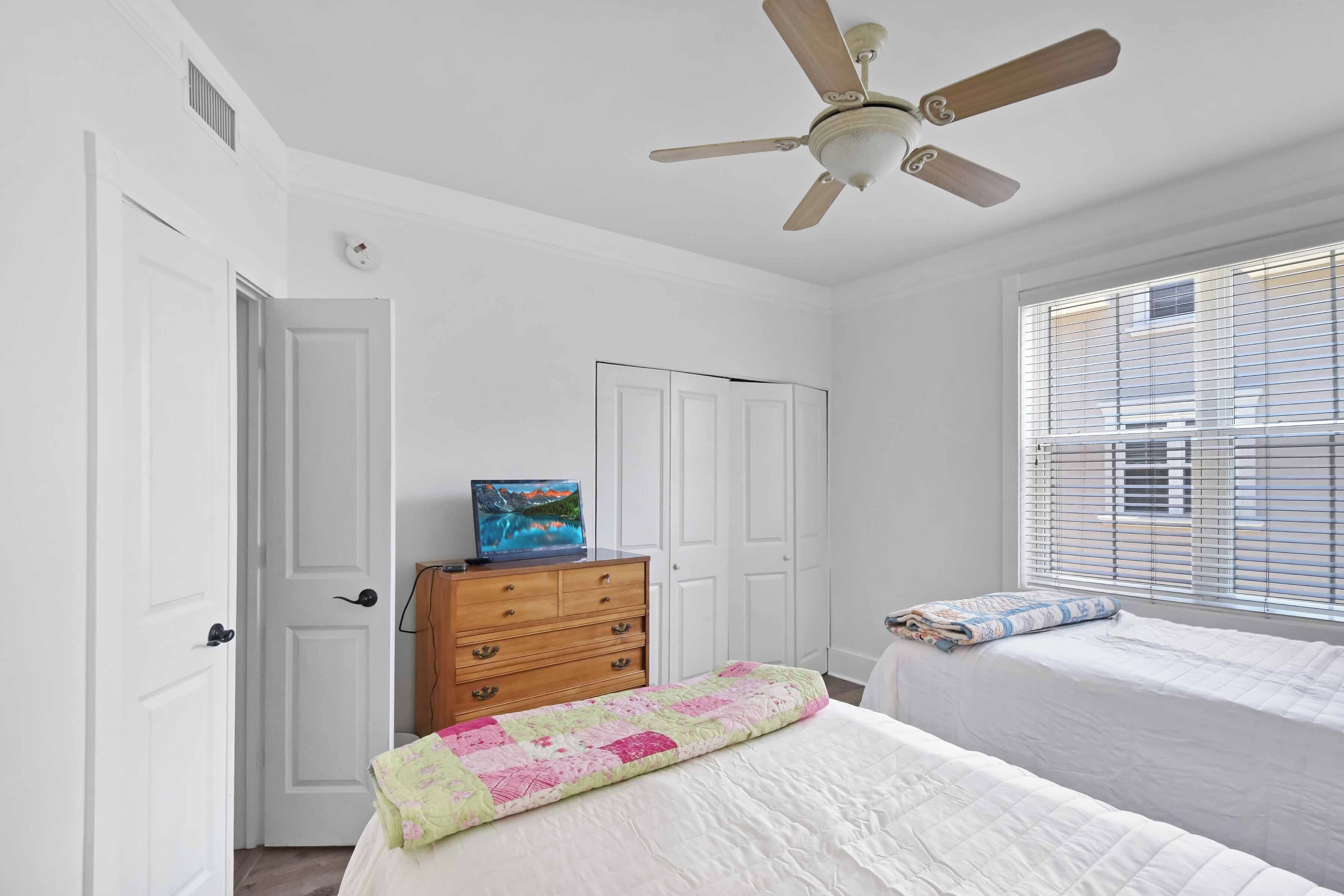 A bedroom with a bed, a dresser, a ceiling fan, and a window with blinds.