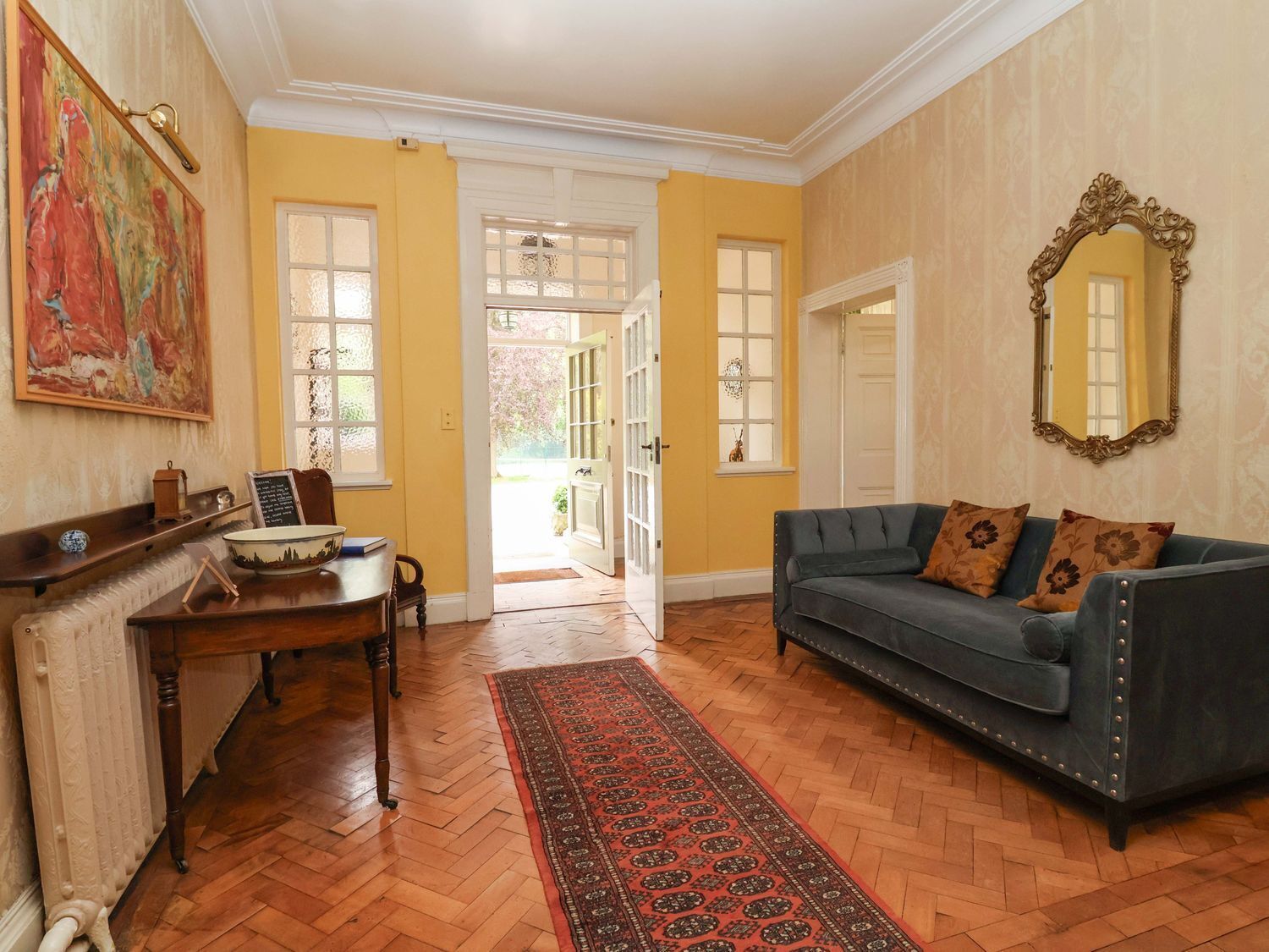 A room with a blue sofa, wooden floor, a radiator, a table with a bowl and book, and a door leading outside.