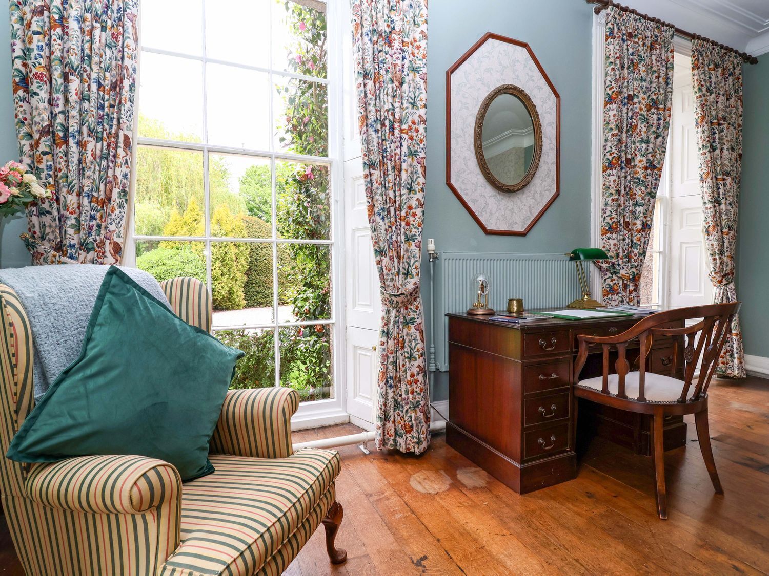 A room with a large window, a desk with drawers, a chair, and a striped sofa.