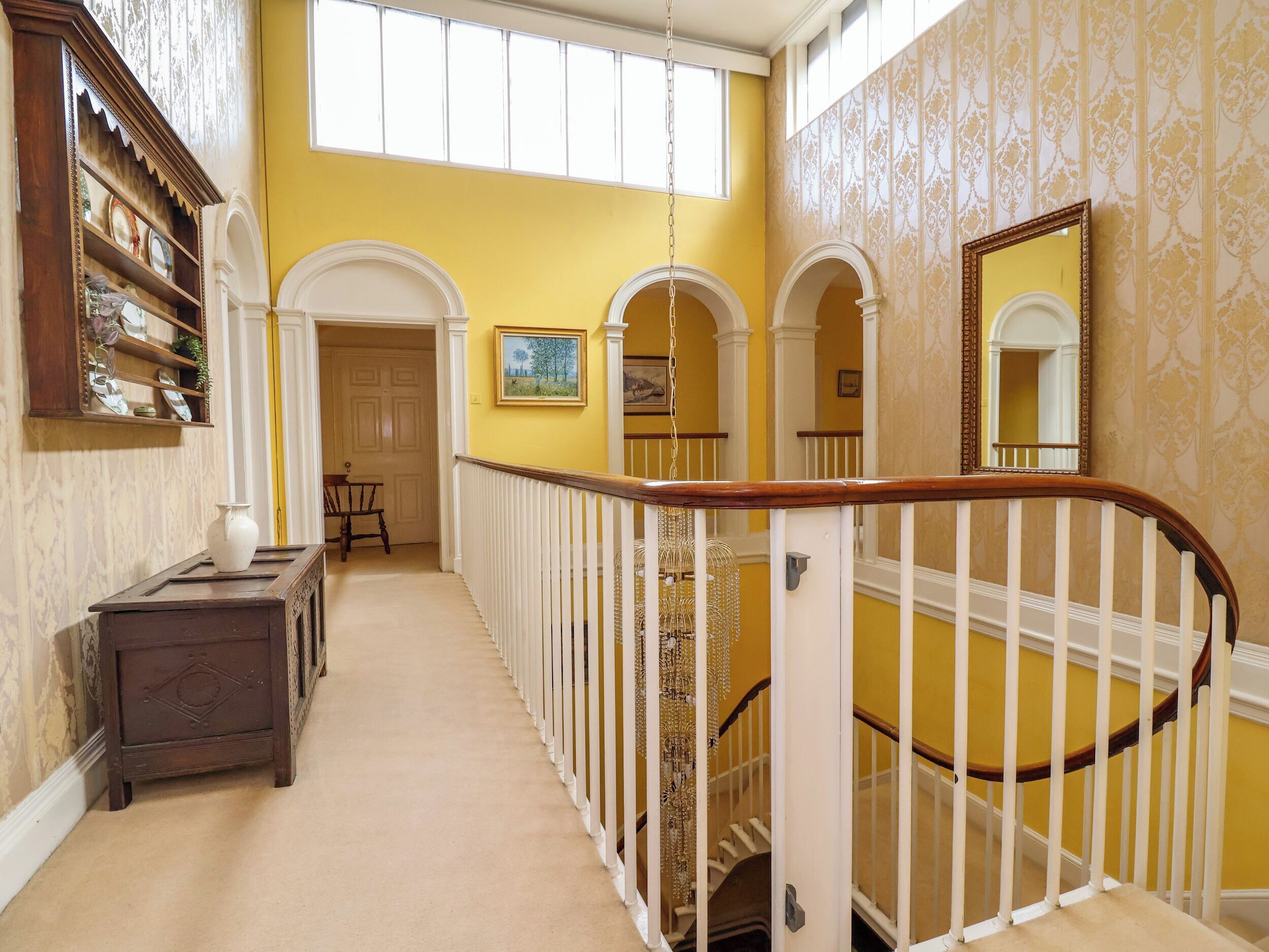 Un pasillo con una escalera, un candelabro y un espejo en la pared.