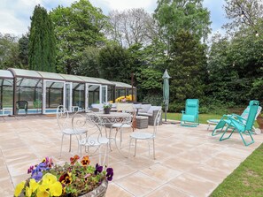 A covered patio with outdoor furniture, a greenhouse, and a flower bed. - Parkfields House (Stoke-on-Trent)