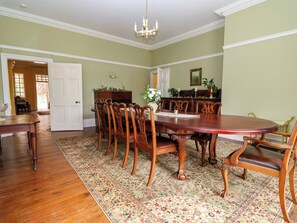 A dining room with a large wooden table, matching chairs, a chandelier, and a patterned rug.