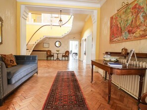 Amplia sala de estar con sofá azul, mesa de centro de madera, alfombra roja con estampado, escalera que conduce a un piso superior y un cuadro grande en la pared.
