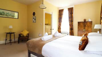 A hotel room with a bed, a chair, a small table, a lamp, a painting, and a wooden cabinet.