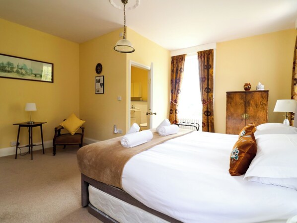 A hotel room with a bed, a chair, a small table, a lamp, a painting, and a wooden cabinet.